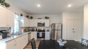 A modern kitchen with white cabinets, stainless steel appliances, and a dark wooden dining table. - Pool house with hot tub! (Houston)