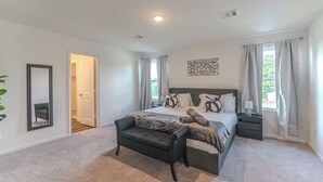 A bedroom with a bed, a bench, a nightstand, a mirror, and a window with curtains. - Pool house with hot tub! (Houston)