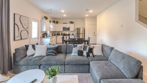 A modern living room with a grey sectional sofa, a white coffee table, and a dining area with a black table and chairs. - Pool house with hot tub! (Houston)