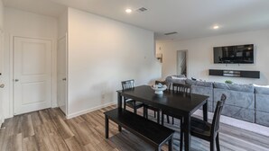 A modern dining area with a dark wooden table and benches, a gray sofa, and a mounted TV. - Pool house with hot tub! (Houston)