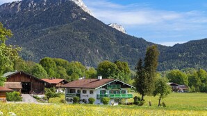 Paisaje montañoso con una casa que tiene un balcón y un campo de flores amarillas en primer plano.