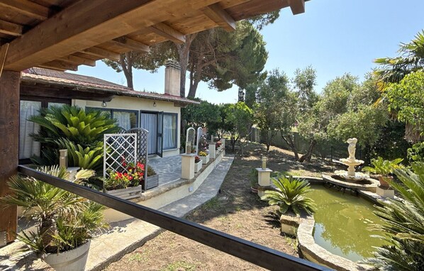 A covered outdoor area with a garden, a fountain, and a pathway leading to a house with a tiled roof. - Casa Luigina, in a quiet area and a stone's throw from the center of Porto Azzurro (Porto Azzurro)