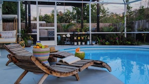 A poolside area with wooden lounge chairs, a wicker basket with fruits, and a book. - 3BR Open-Plan Retreat w/ Heated Pool, Screened Patio & Grill – Melbourne (Melbourne)