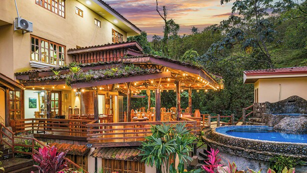 Un restaurante con terraza, piscina y abundante vegetación.
