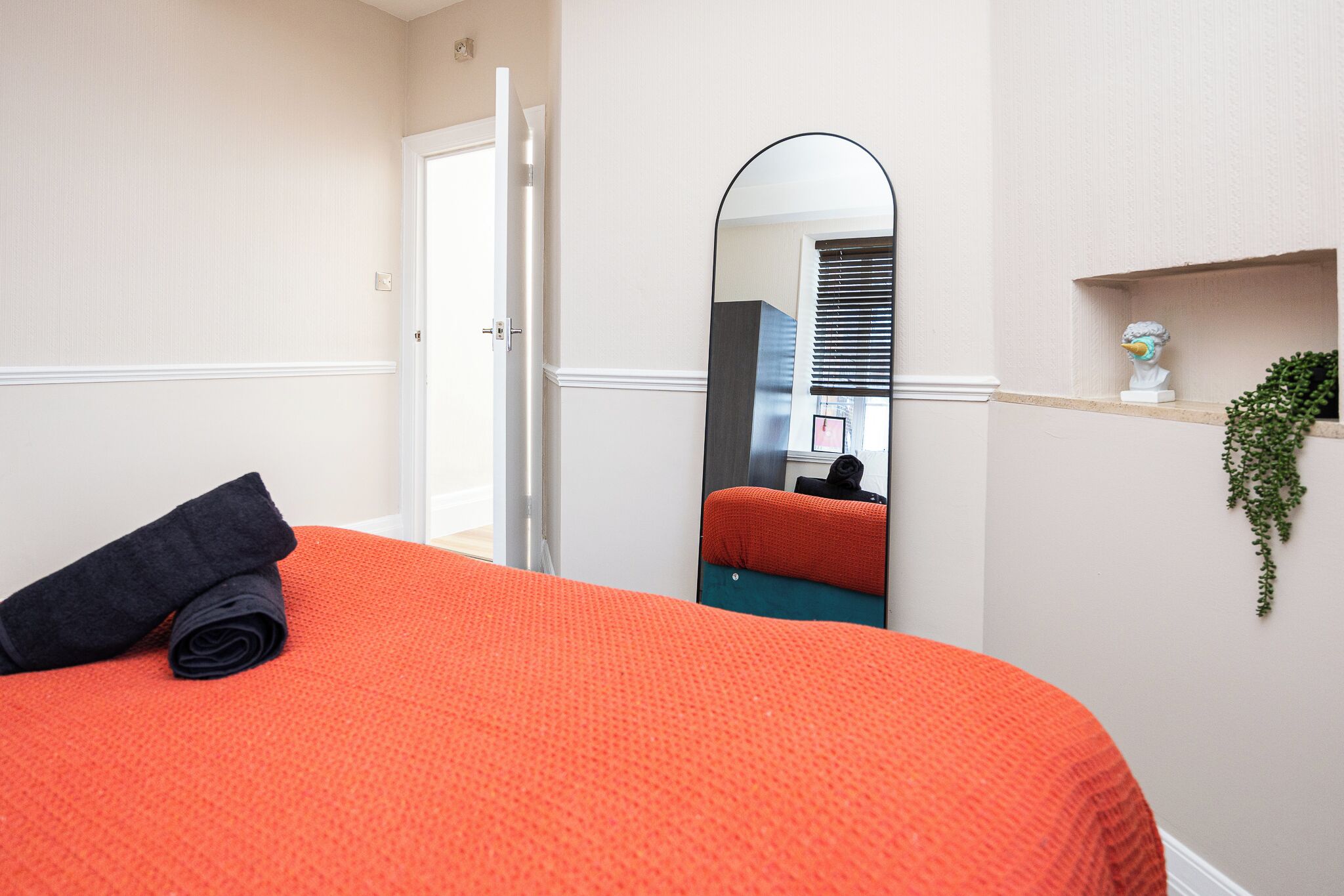 Ein Hotelzimmer mit einem Bett, einem Spiegel, einer Tür und einem kleinen Regal mit einer Pflanze.