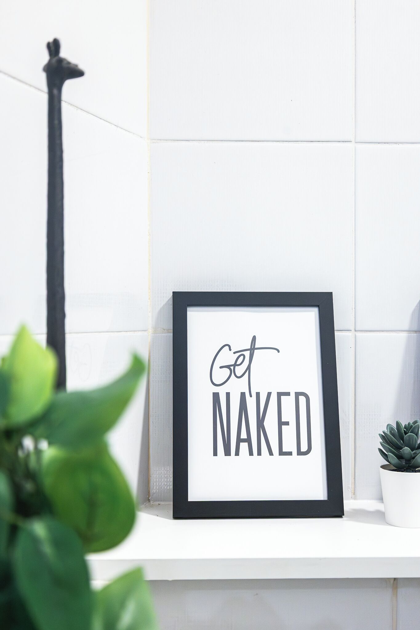 A framed sign with the text "Get Naked" on a white shelf.