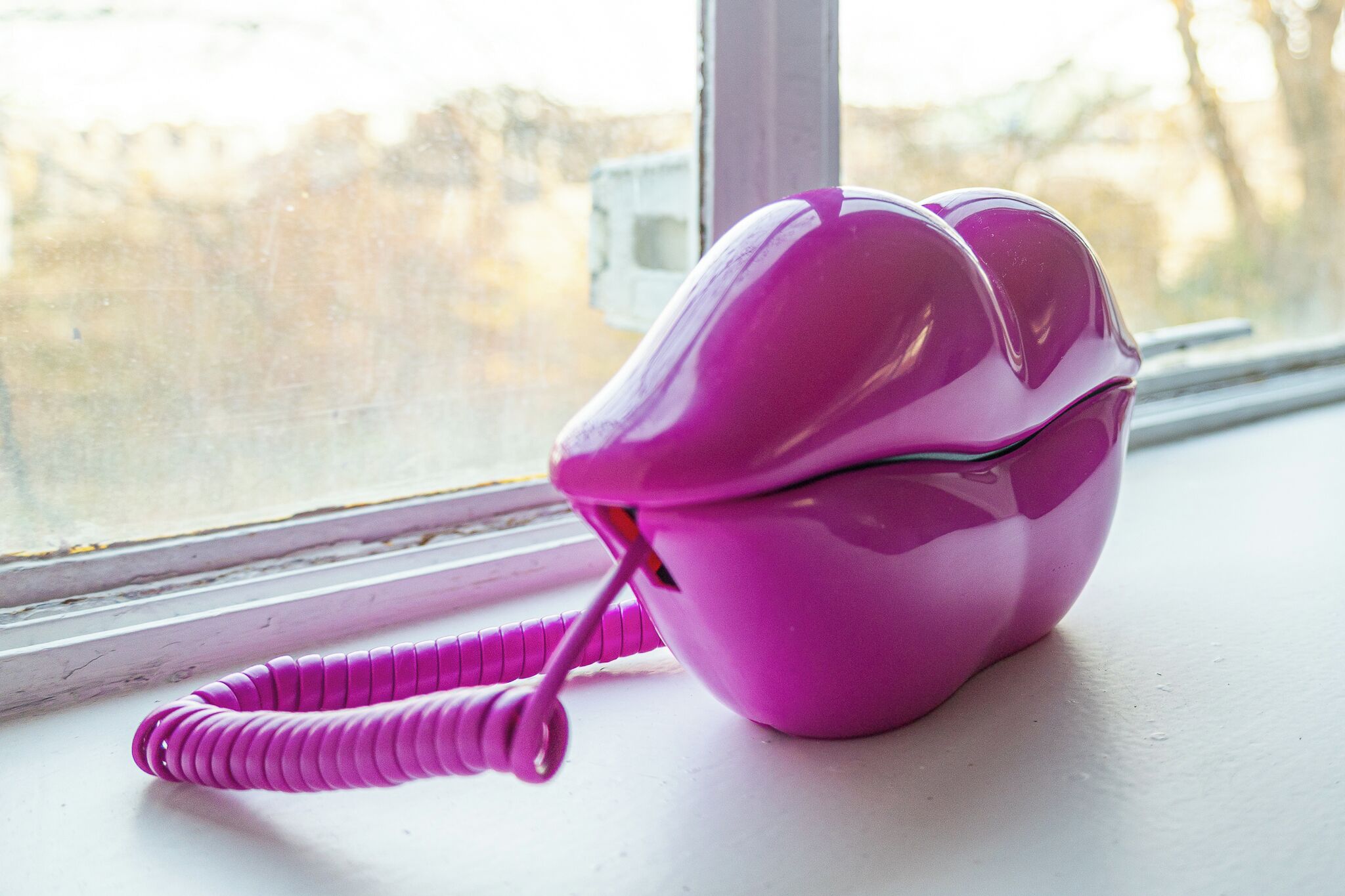 A pink telephone on a windowsill.