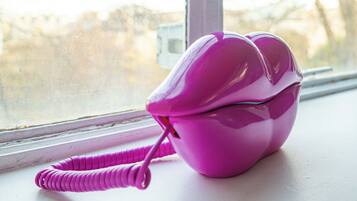 A pink telephone on a windowsill.