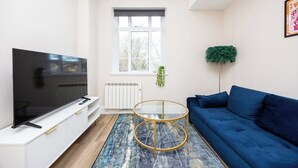 Una sala de estar moderna con un televisor de pantalla plana, un sofá azul, una mesa de centro de vidrio y un radiador.
