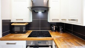 Una cocina con armarios blancos, estufa negra, microondas y cafetera.