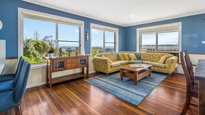 Un salón amplio con un sofá grande, una mesa de centro y vistas a zonas verdes a través de amplias ventanas.