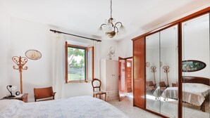 Un dormitorio con cama, armario, espejo y ventana.