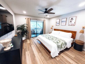 Une chambre à coucher avec un lit, un ventilateur de plafond, une télévision, une plante et un balcon avec vue.