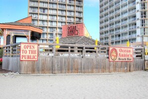Une clôture en bois avec des panneaux indiquant « Ocean Annie’s Beach Bar » et « OUVERT AU PUBLIC ».