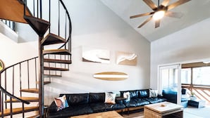 A modern living room with a black leather sofa, wooden coffee table, and a spiral staircase.
