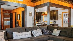 Ein gemütliches Wohnzimmer mit einer Eckcouch, einem Couchtisch und einer Küche im Hintergrund.