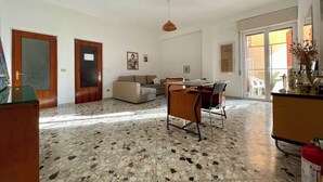 A spacious living area with a tiled floor, a sofa, a dining table with chairs, and a kitchen area with a stove and cabinets. - The Collector's Home - Station & Park view (Unknown)