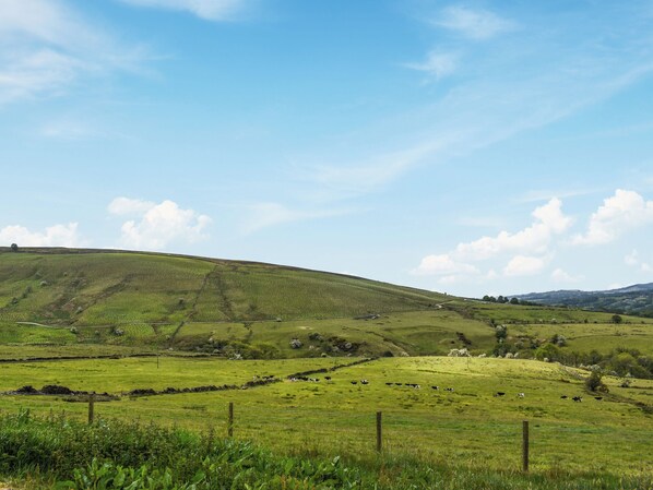A rural landscape with rolling hills, a fenced field, and a clear sky.