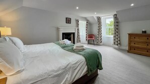 A bedroom with a bed, a dresser, a chair, a fireplace, and a window with curtains.