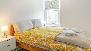A bedroom with a bed, a nightstand, a lamp, and a window with a view of a brick building. - 3 bedroom accommodation in Skipton (Skipton)