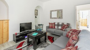 A modern living room with a grey sofa, a black coffee table, a flat-screen TV, and a small side table with a lamp. - 3 bedroom accommodation in Skipton (Skipton)