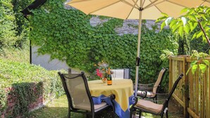 Une terrasse extérieure avec une table et des chaises, un parasol jaune et un mur recouvert de lierre vert.