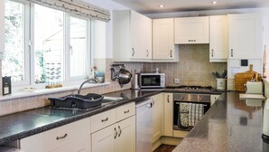 Une cuisine moderne avec des armoires blanches, un comptoir en granit, un four encastré et une fenêtre donnant sur un paysage verdoyant.