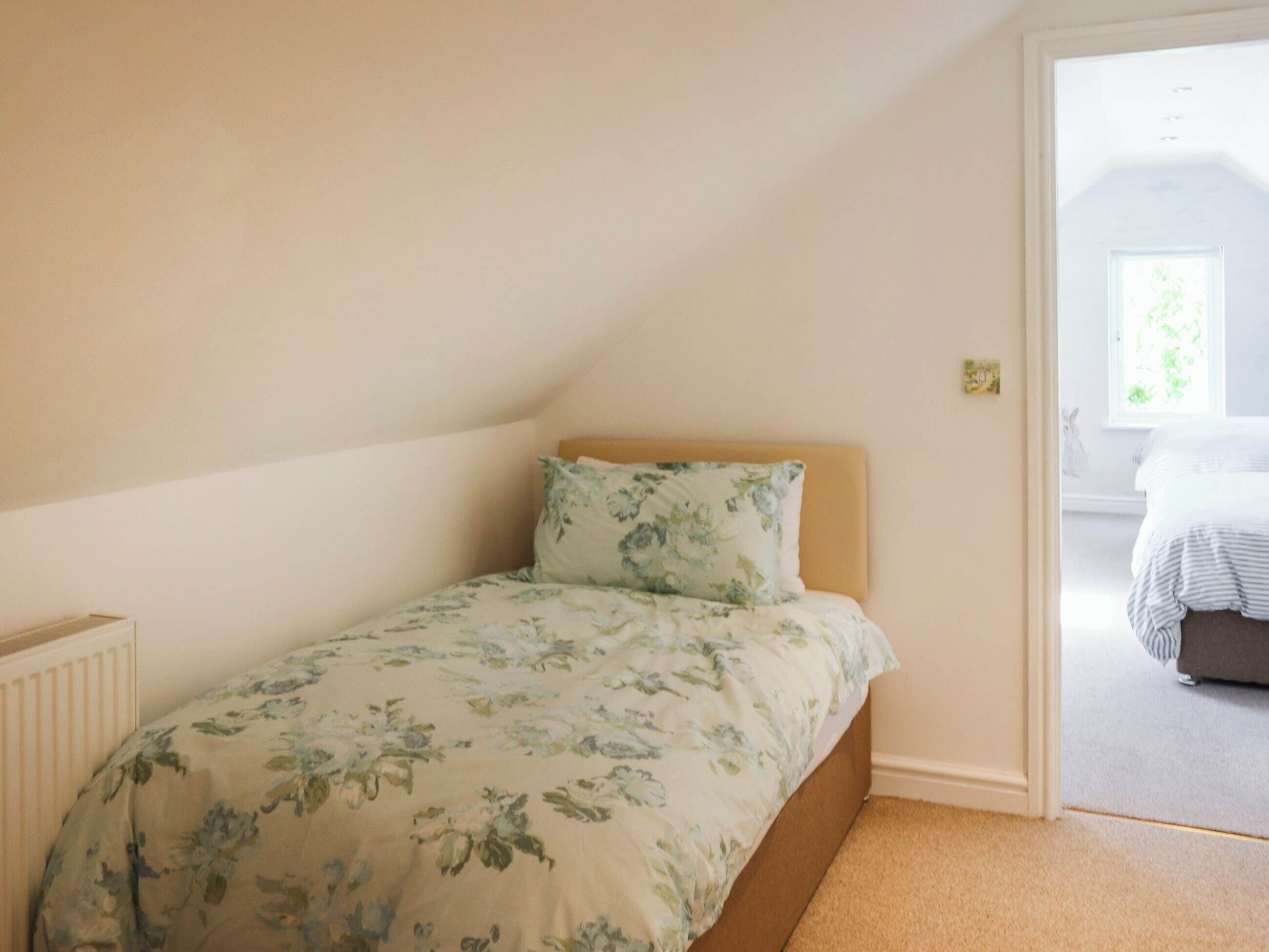 A small, single-bed room with a floral bedspread and a wooden headboard.