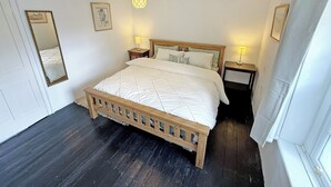 A bedroom with a wooden bed, two bedside tables with lamps, a mirror, and a framed picture on the wall. - 2 bedroom accommodation in Cheltenham (Cheltenham)