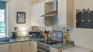 Une cuisine compacte avec des meubles blancs, un four à micro-ondes, une bouilloire et un grille-pain. Il y a un calendrier accroché au mur et une fenêtre donnant sur un paysage verdoyant.