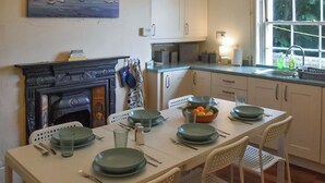 Un coin repas avec une table dressée pour quatre personnes, une cheminée et une fenêtre donnant sur la mer.