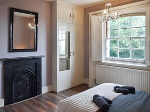 A bedroom with a fireplace, a large window with a view, and a chandelier. - 2 bedroom accommodation in Lowestoft (Lowestoft)