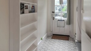 Un couloir étroit avec une porte blanche, un radiateur et des carreaux de sol à motifs.