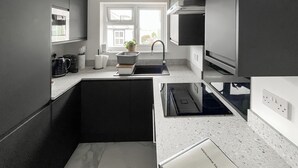 Eine moderne Küche mit dunklen Schränken, einem eingebauten Backofen und einem Fenster, das für natürliches Licht sorgt.