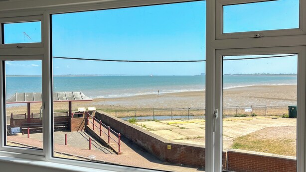 Blick aus einem Fenster auf einen Strand mit einer Umzäunung und einem Schild, auf dem 'INDIAN' steht.