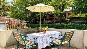 Eine Terrasse mit Tisch, zwei Stühlen, einem Sonnenschirm und einem Blumentopf.