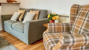 Ein Wohnzimmer mit grauem Sofa, Ohrensessel mit Karomuster und einem kleinen Tisch mit Topfpflanze.