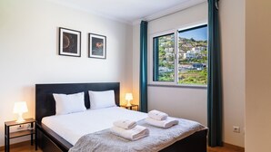 Une chambre d’hôtel avec un lit, deux lampes de chevet, une fenêtre donnant sur des immeubles et deux tableaux encadrés accrochés au mur.