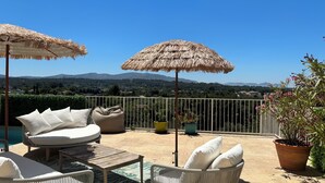 Eine Terrasse mit Korbmöbeln, einem Reetdachschirm und Blick auf ferne Berge.