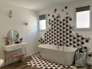 Une salle de bain moderne avec une baignoire sur pieds, un meuble-lavabo doté d’un miroir rond et un motif géométrique hexagonal sur les murs et le sol.