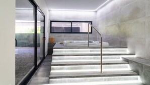 Un interior moderno con una escalera que conduce a un área de spa, con entrada por una puerta de cristal y un ventanal grande.