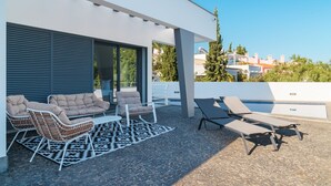 Un patio moderno al aire libre con mobiliario de mimbre, un tapete estampado y una zona de piscina.