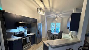 A modern kitchen with dark cabinetry, stainless steel appliances, and a central island with bar stools. - Beach House in the Woods, Fire Pit Deck/Daytona 3/2 Large Fenced in Home. (Daytona Beach)