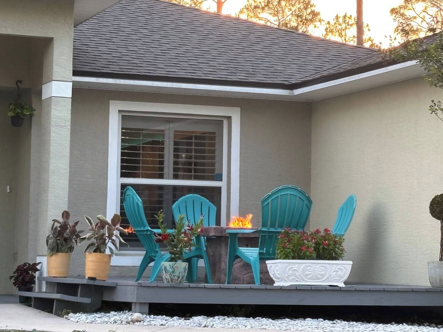 A house with a covered patio area featuring a table and chairs, potted plants, and a fire feature.