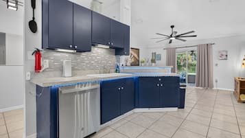 A modern kitchen with dark blue cabinets, a stainless steel dishwasher, and a tiled backsplash.