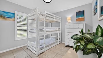 A child's bunk bed with a window, a bedside table with a lamp, and a potted plant.