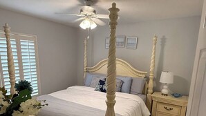 A four-poster bed with a canopy, a bedside table with a lamp, and a dresser with a vase of flowers. - Beach House in the Woods, Fire Pit Deck/Daytona 3/2 Large Fenced in Home. (Daytona Beach)