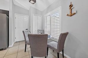 A dining area with a table and two chairs, a window with blinds, and a wall-mounted anchor decoration.