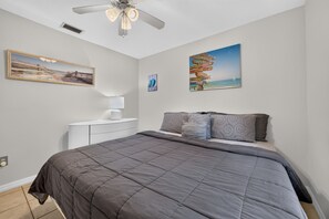 Un dormitorio con una cama, una mesita de noche, un ventilador de techo y decoración en la pared.