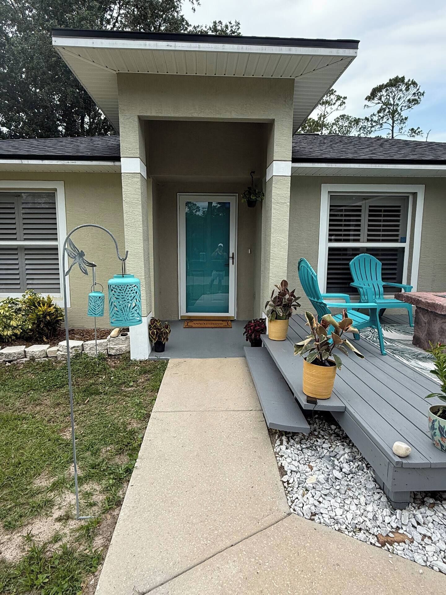 A house with a covered porch, a door, and outdoor seating with chairs and planters.